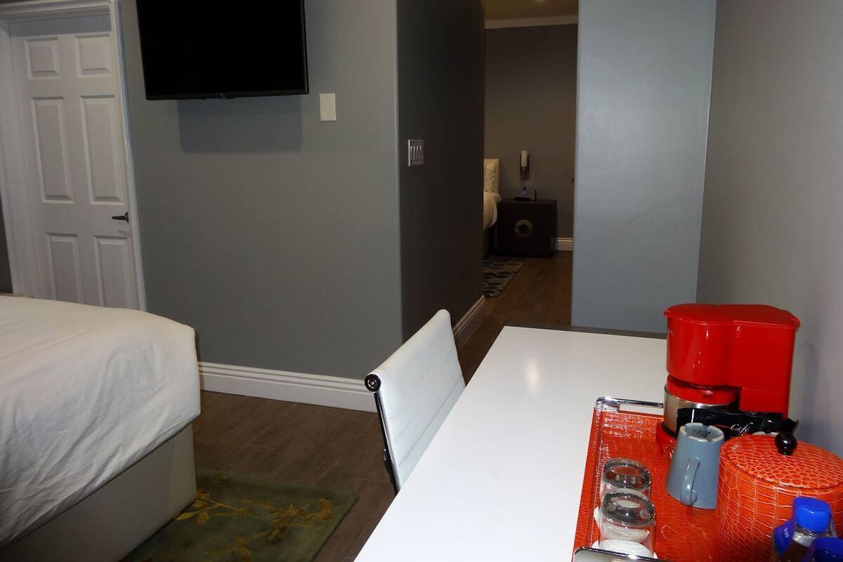 A hotel room with a bed, a TV mounted on the wall, a coffee maker, and a table with various items.