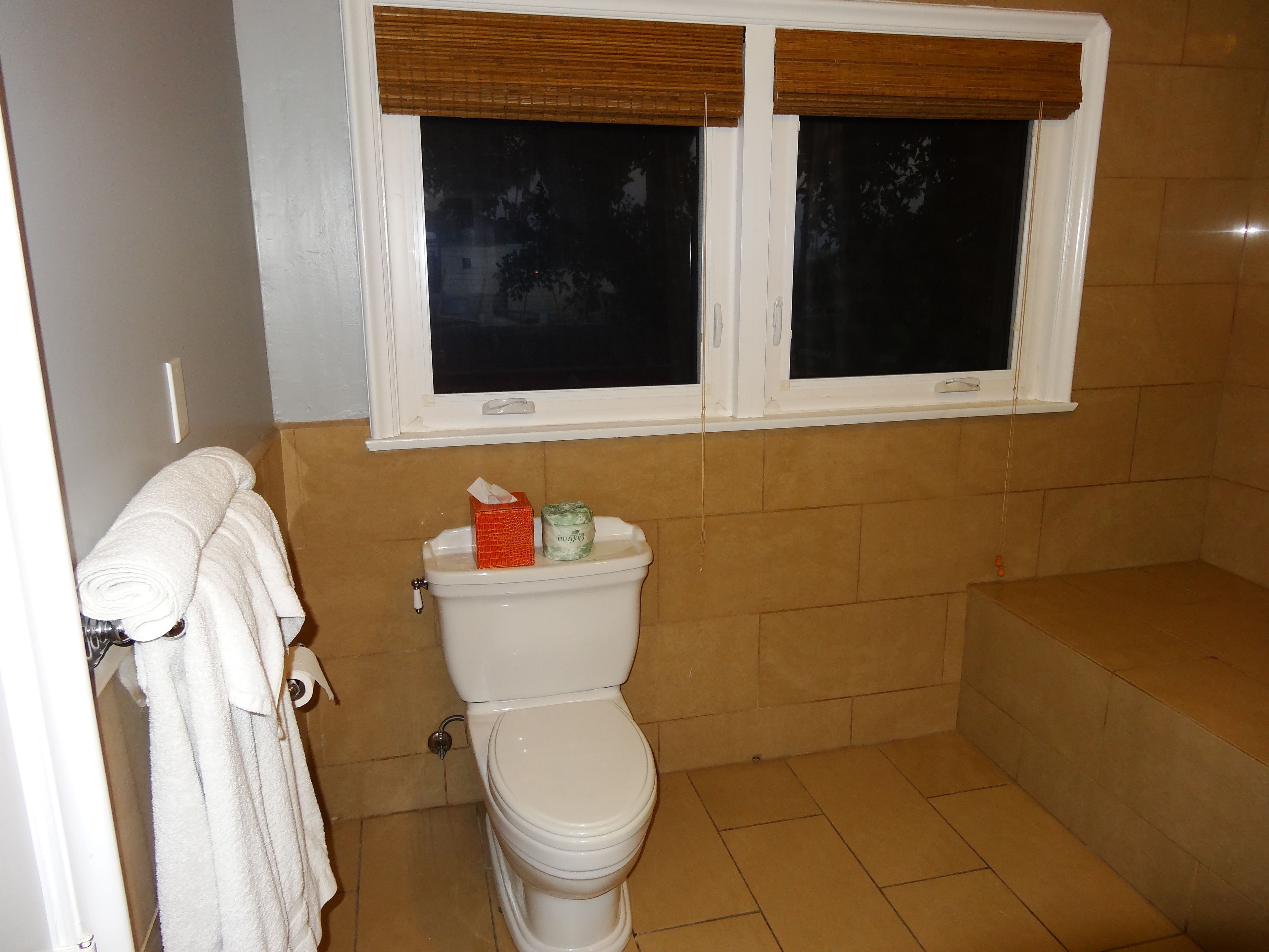 Un baño con inodoro, ventana con persianas y bañera.