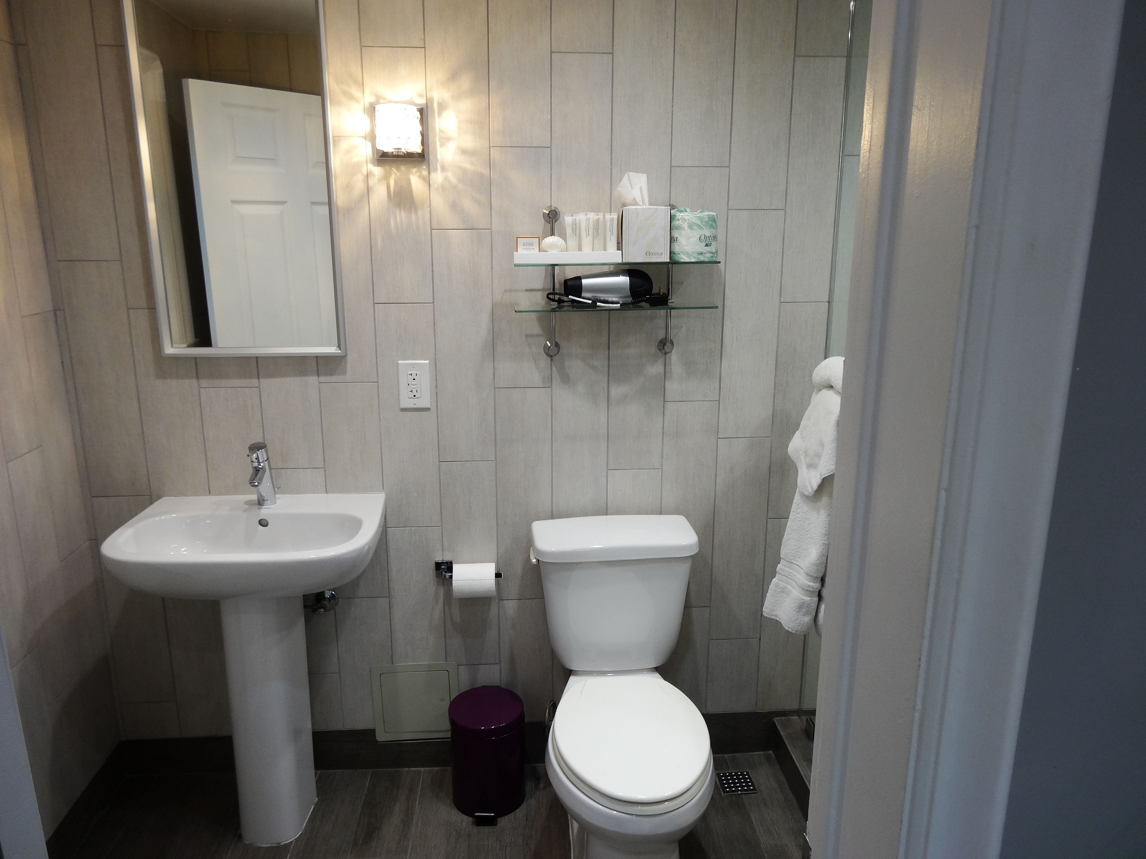A bathroom with a white sink, toilet, and a glass shelf with toiletries.
