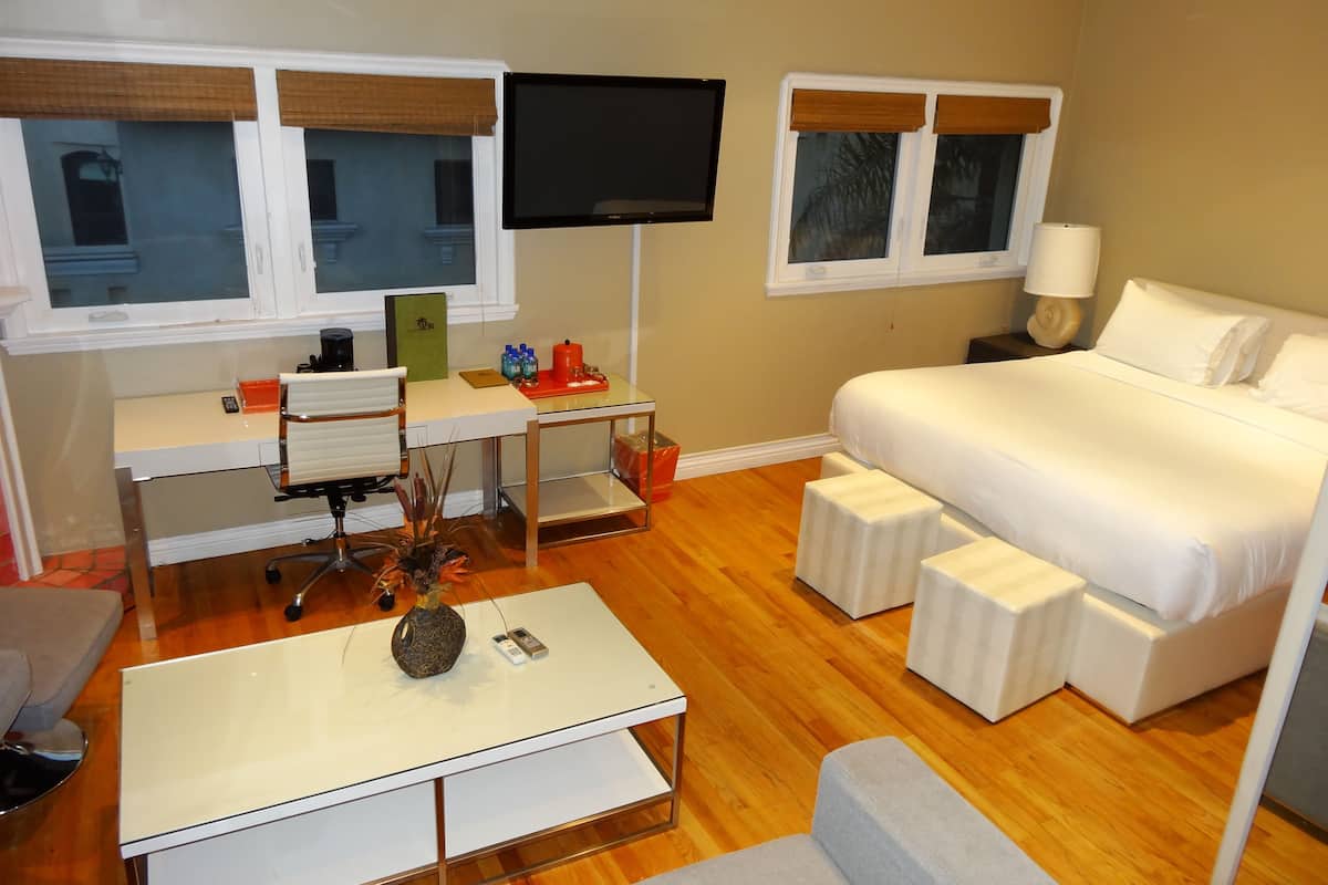 A hotel room with a bed, a desk with a chair, a TV, and a small table with a vase.