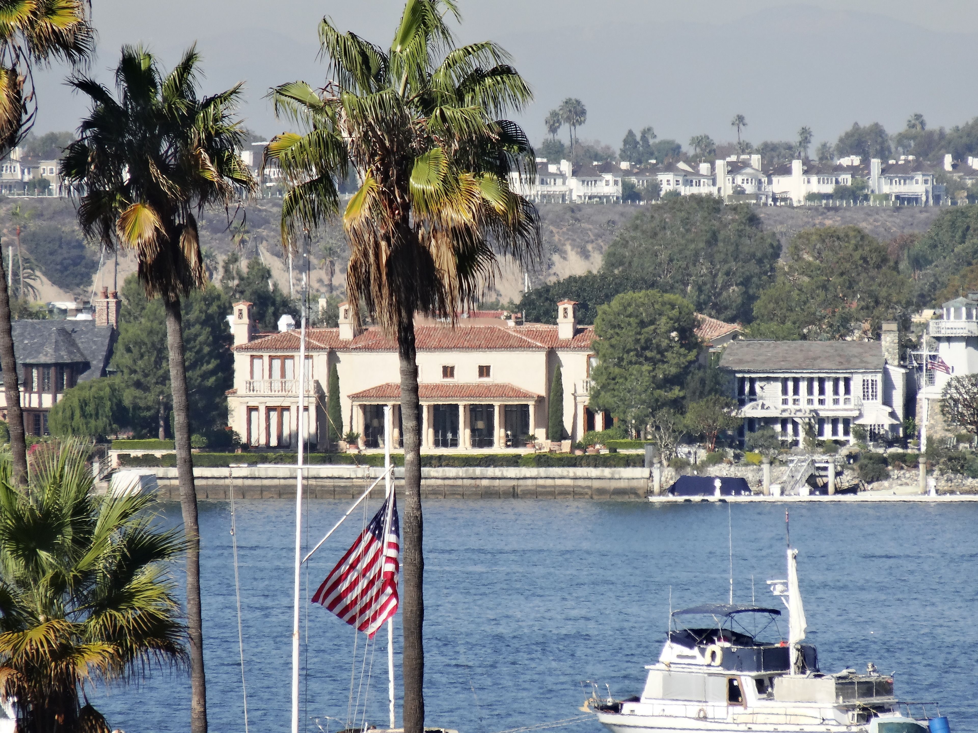 A waterfront property with a large house, palm trees, and a boat docked nearby.