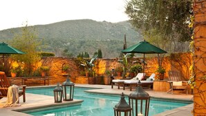 Un área junto a la piscina con sillones de descanso, plantas en macetas y faroles.