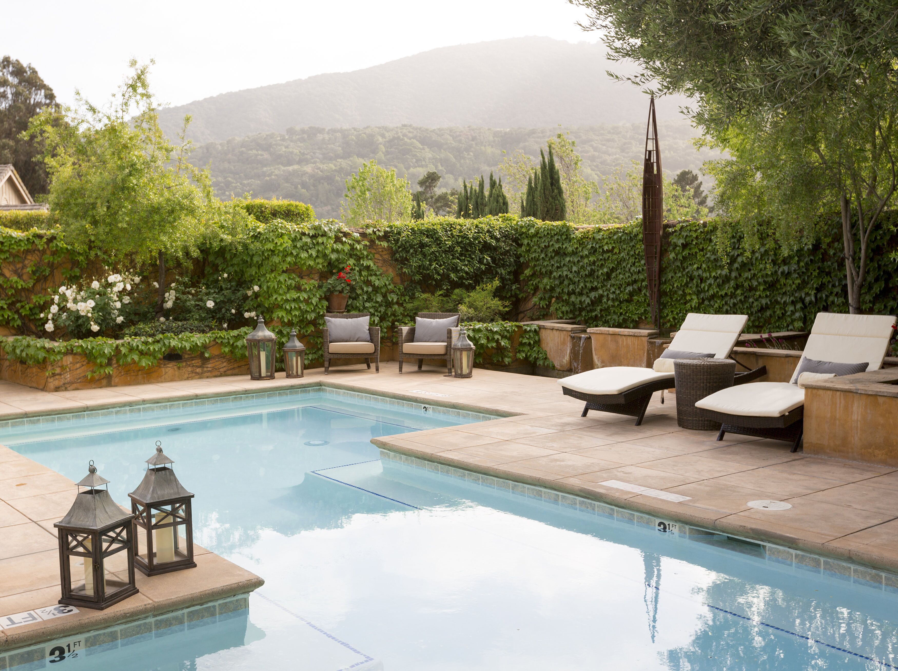 A pool area with lounge chairs and lanterns, surrounded by greenery and a mountainous backdrop.