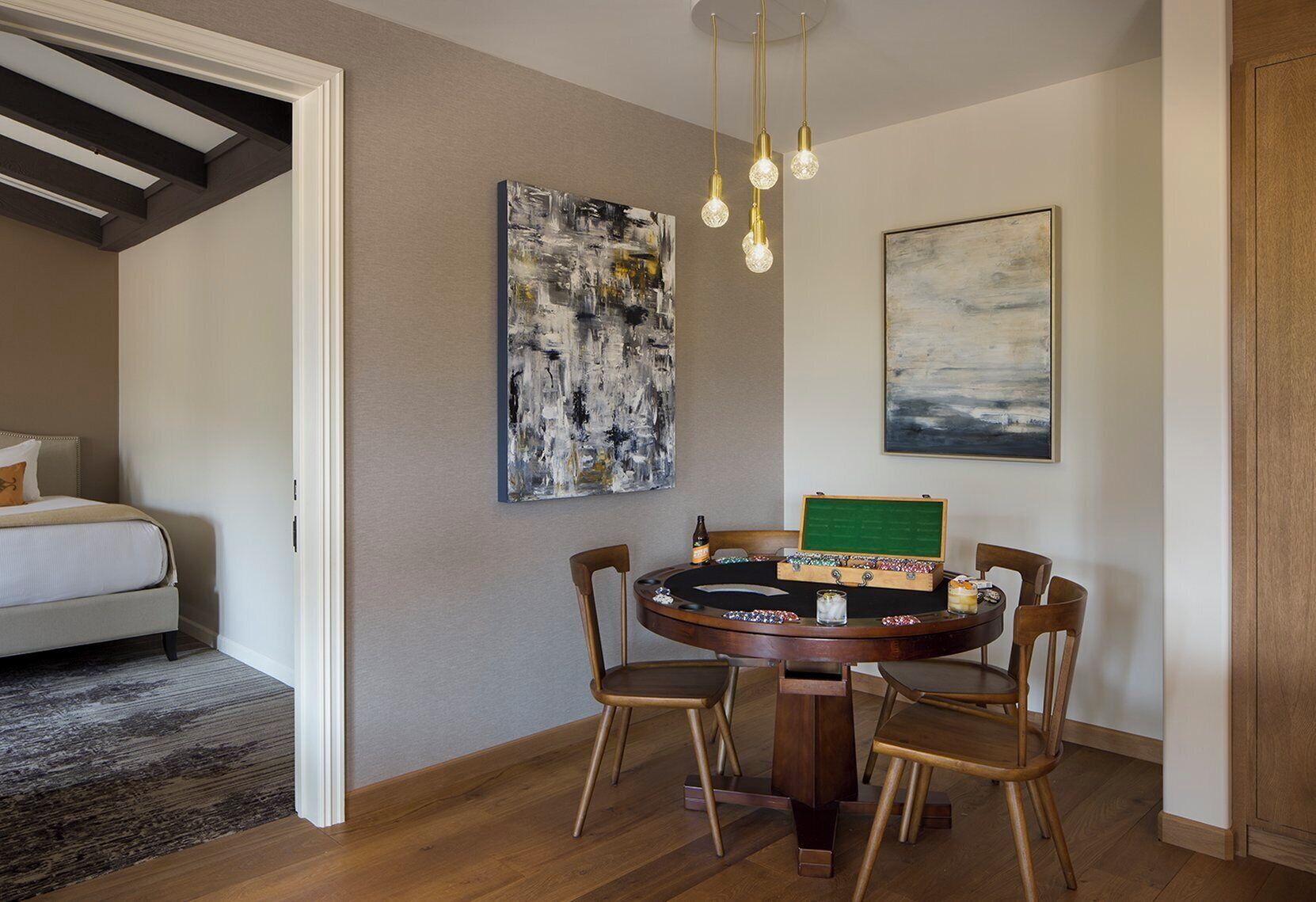 A dining area with a round wooden table, four chairs, a green chalkboard, and two abstract paintings on the walls.
