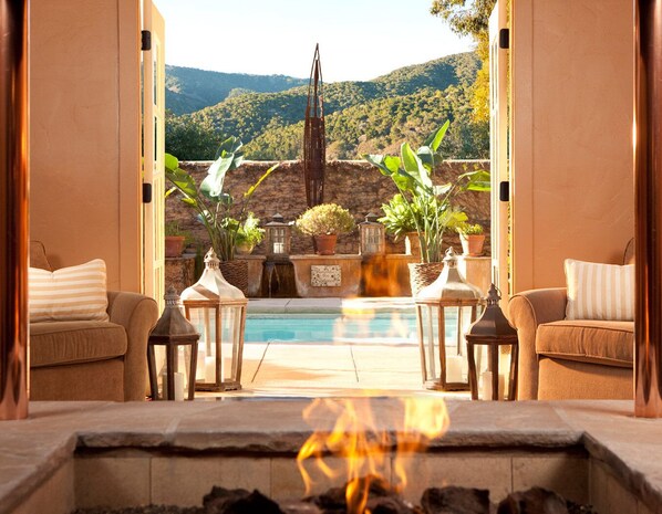 A cozy outdoor seating area with a fireplace, a pool, and potted plants. - Bernardus Lodge & Spa (Carmel Valley)