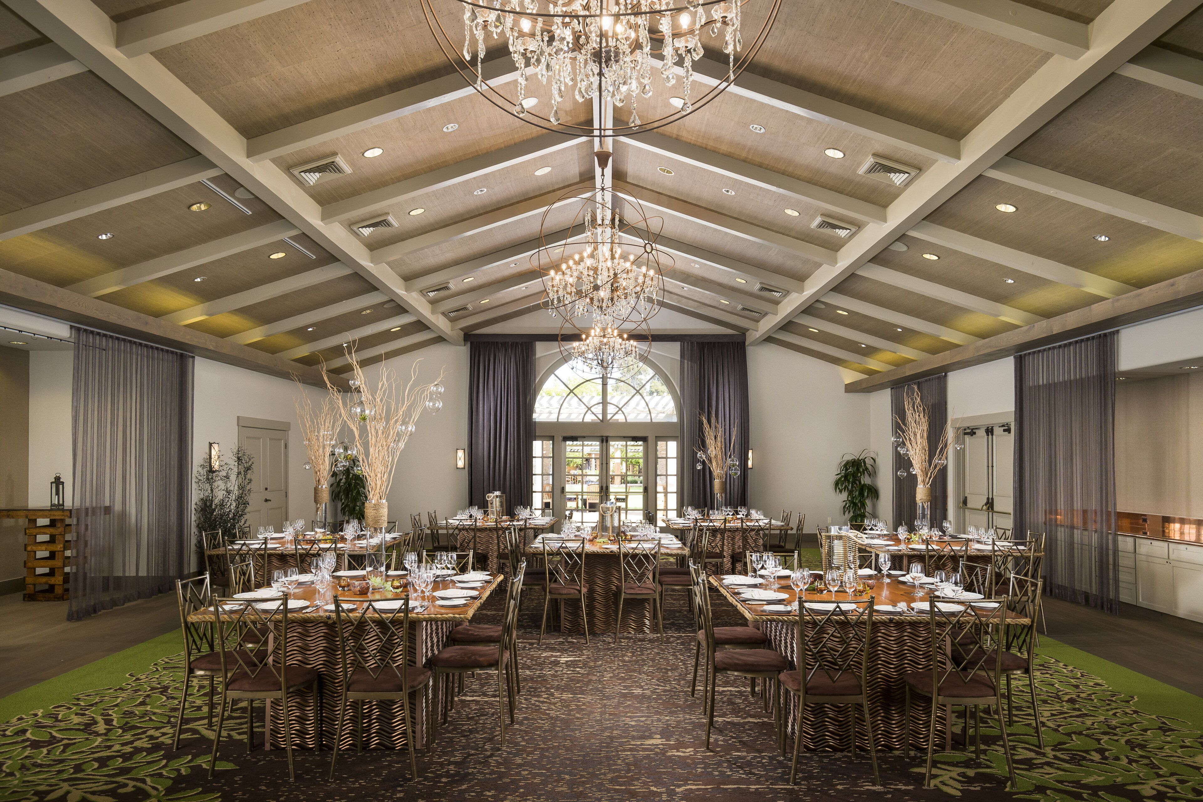 Un amplio salón de banquetes con techos altos, candelabros y una mesa central dispuesta para un evento formal.