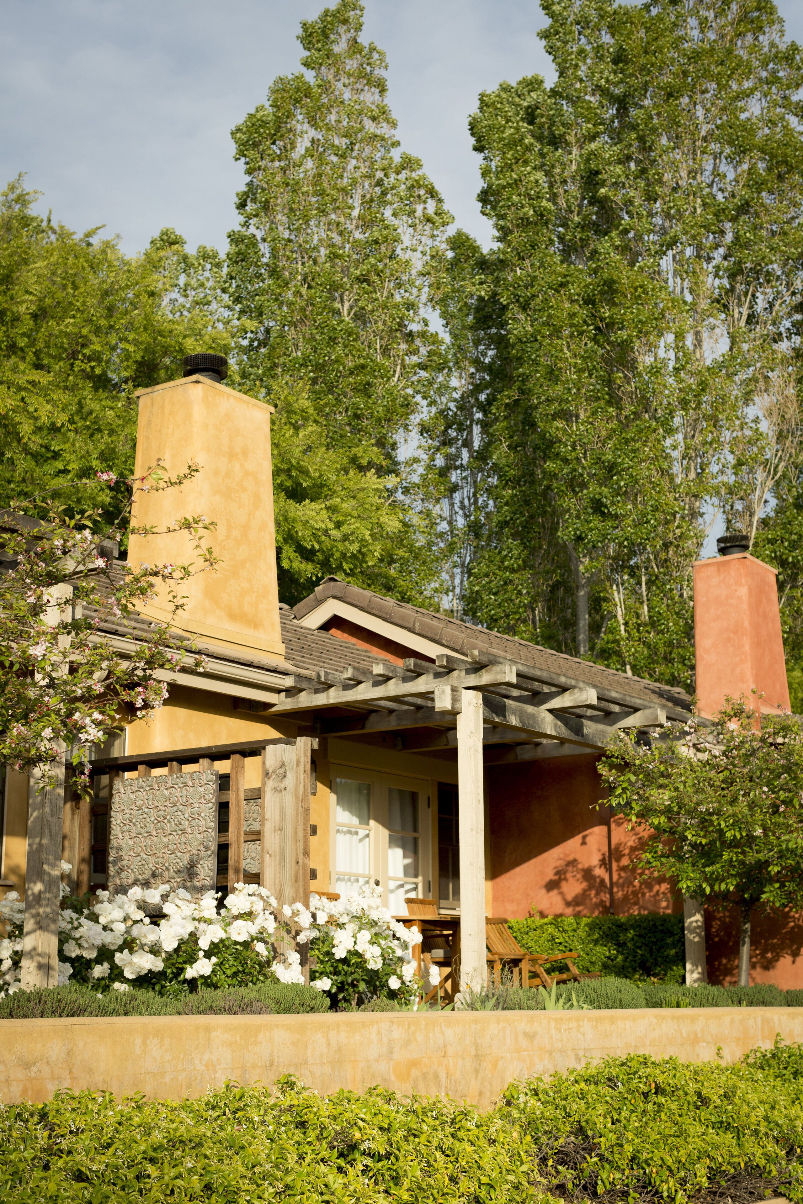 Ein Haus mit einem Steinkamin, einer Holzterrasse und einem Garten mit weißen Blumen.