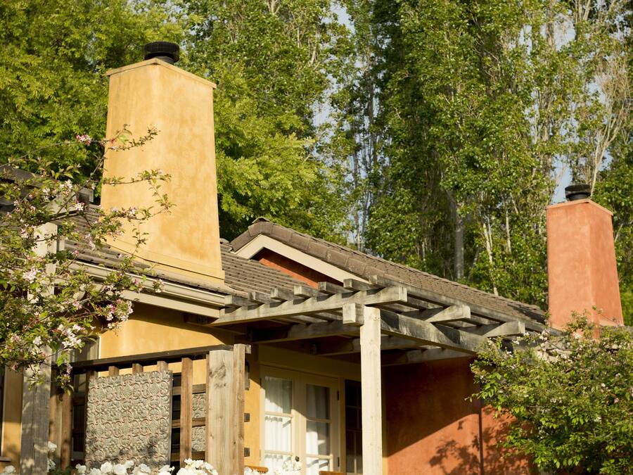 A house with a stone chimney, wooden porch, and a garden with white flowers.