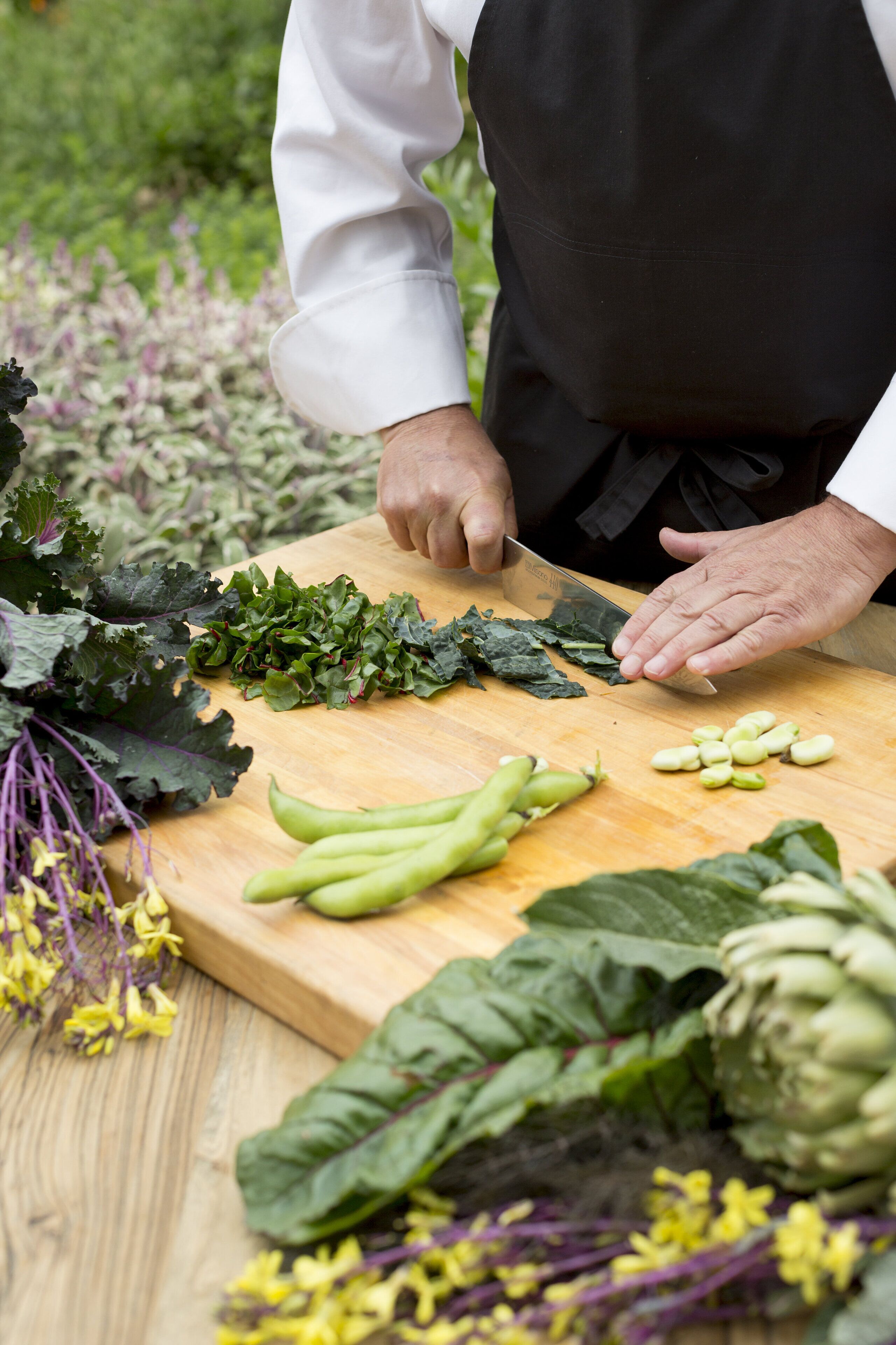 A person chopping leafy greens on a wooden cutting board.