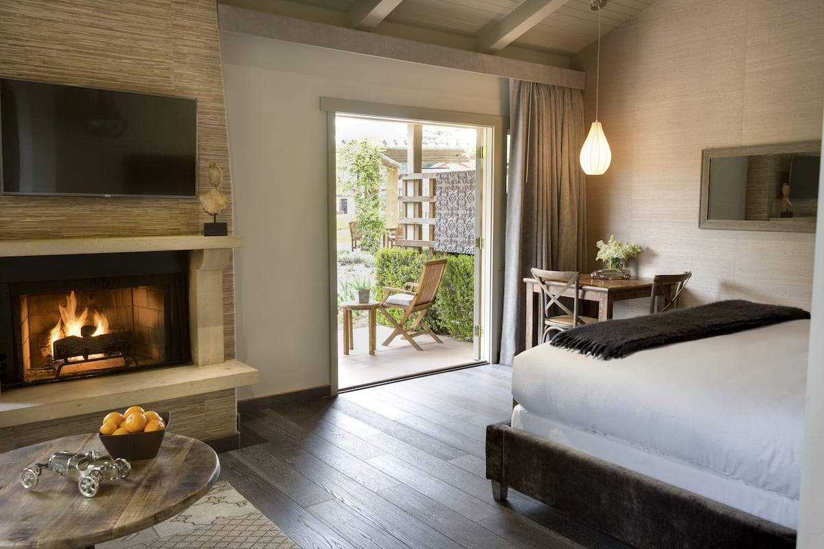 A bedroom with a fireplace, a bed, a desk, and a view of the outdoor patio.