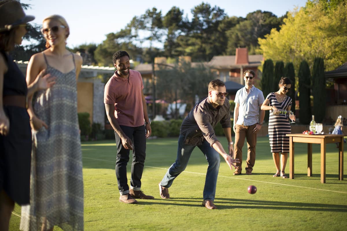 A group of people playing croquet on a well-maintained lawn with a table and chairs nearby.