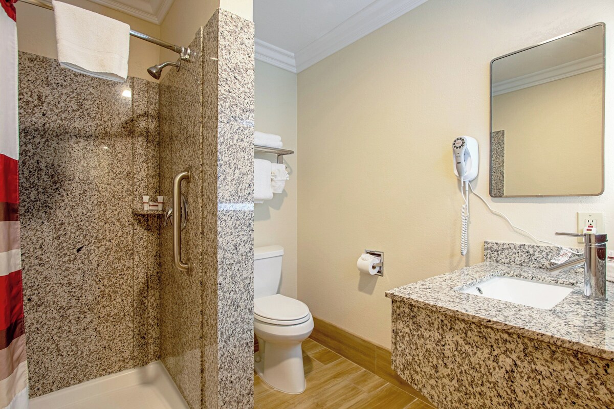 A bathroom with a shower, toilet, sink, and a hairdryer on the wall.