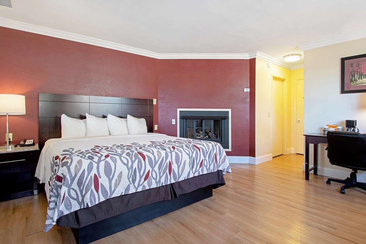 A modern hotel room with a large bed, a fireplace, a desk, and a chair.