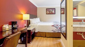 A hotel room with a bed, a desk with a lamp, a coffee maker, and a chair. - Red Roof Inn & Suites Monterey (Monterey)
