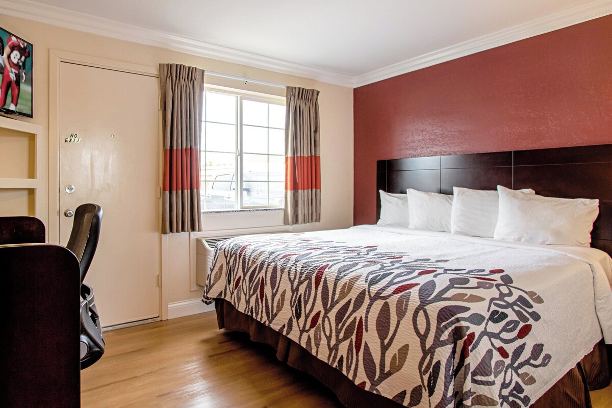 A hotel room with a large bed, a desk, and a window with curtains.