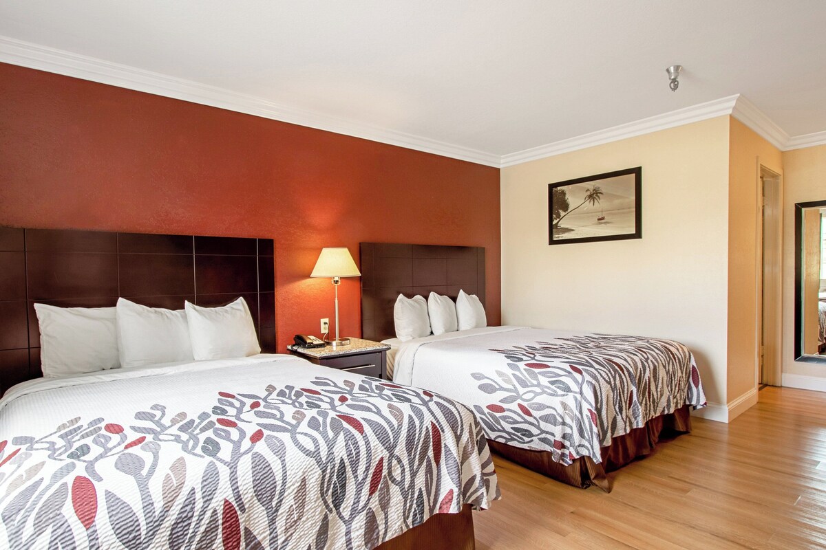 Ein Hotelzimmer mit zwei Betten, einem Nachttisch, einer Lampe und einem gerahmten Bild an der Wand.