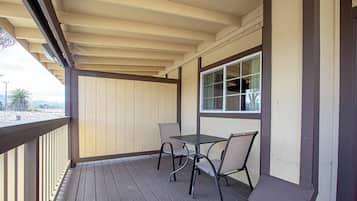 Uma área de estar coberta ao ar livre, com mesa e cadeiras, uma janela e vista para o exterior.