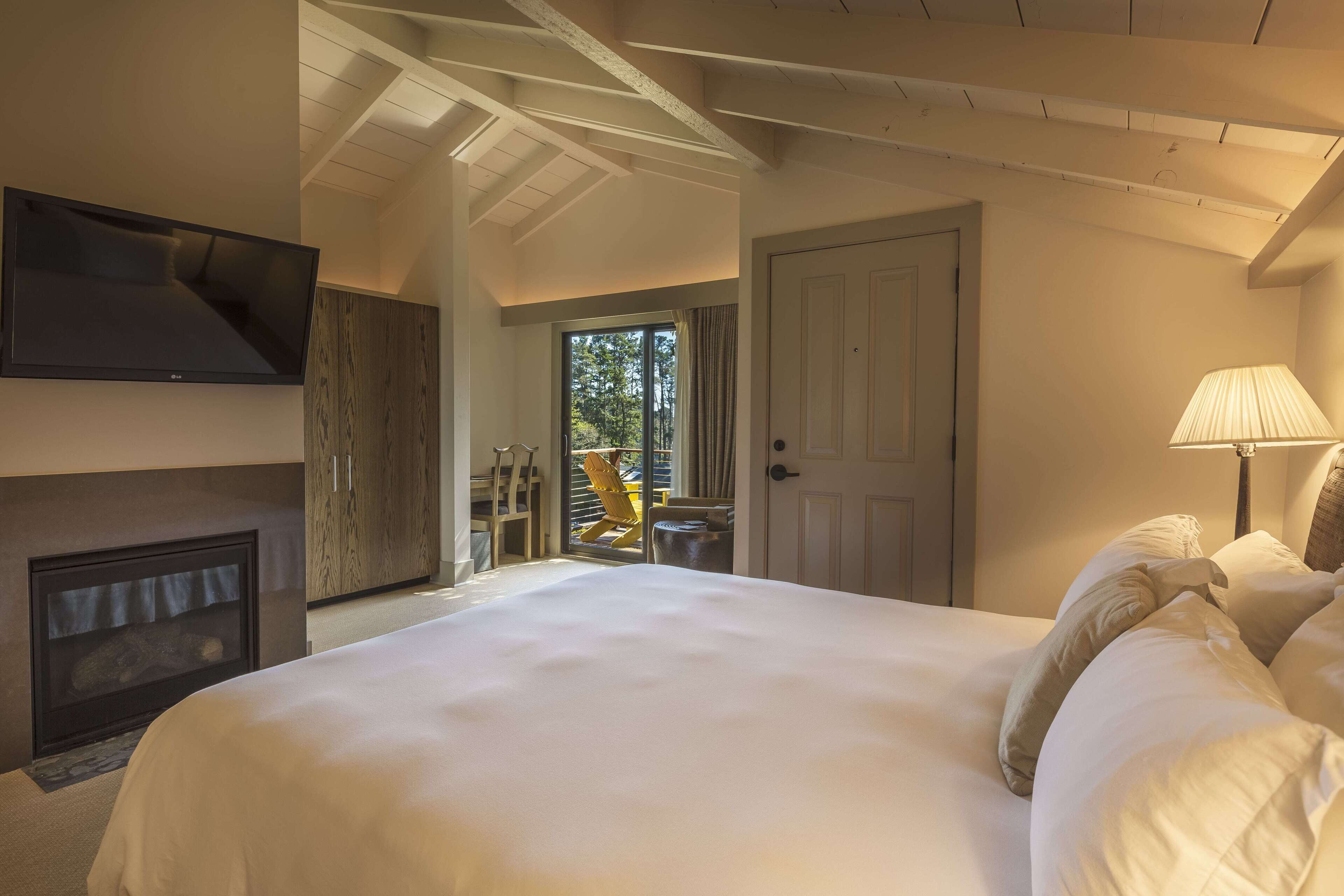 Un dormitorio con una cama grande, un televisor montado en la pared, un armario de madera y una puerta que da a un espacio exterior.