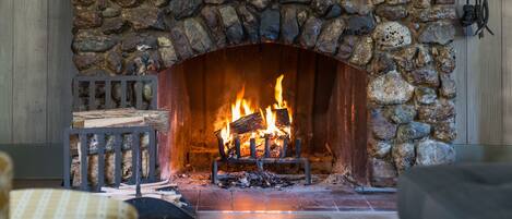 A stone fireplace with a fire burning inside, surrounded by a wooden bench and a rug on the floor.
