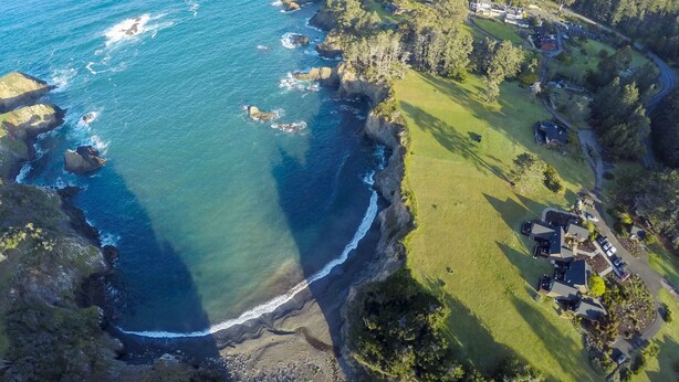 An aerial view of a coastal property with a grassy area, several houses, and a rocky coastline.