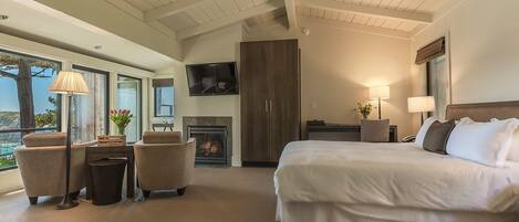 A hotel room with a large bed, a fireplace, a television, and a balcony with a view.