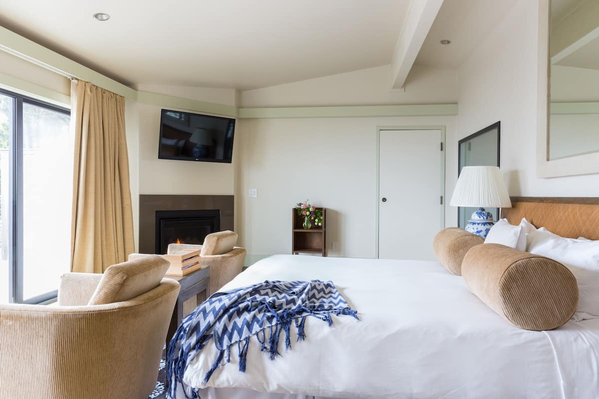 A hotel room with a bed, a television, a fireplace, a chair, and a lamp.