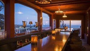 A bar area with a long counter, bar stools, and a view of the landscape through large windows.