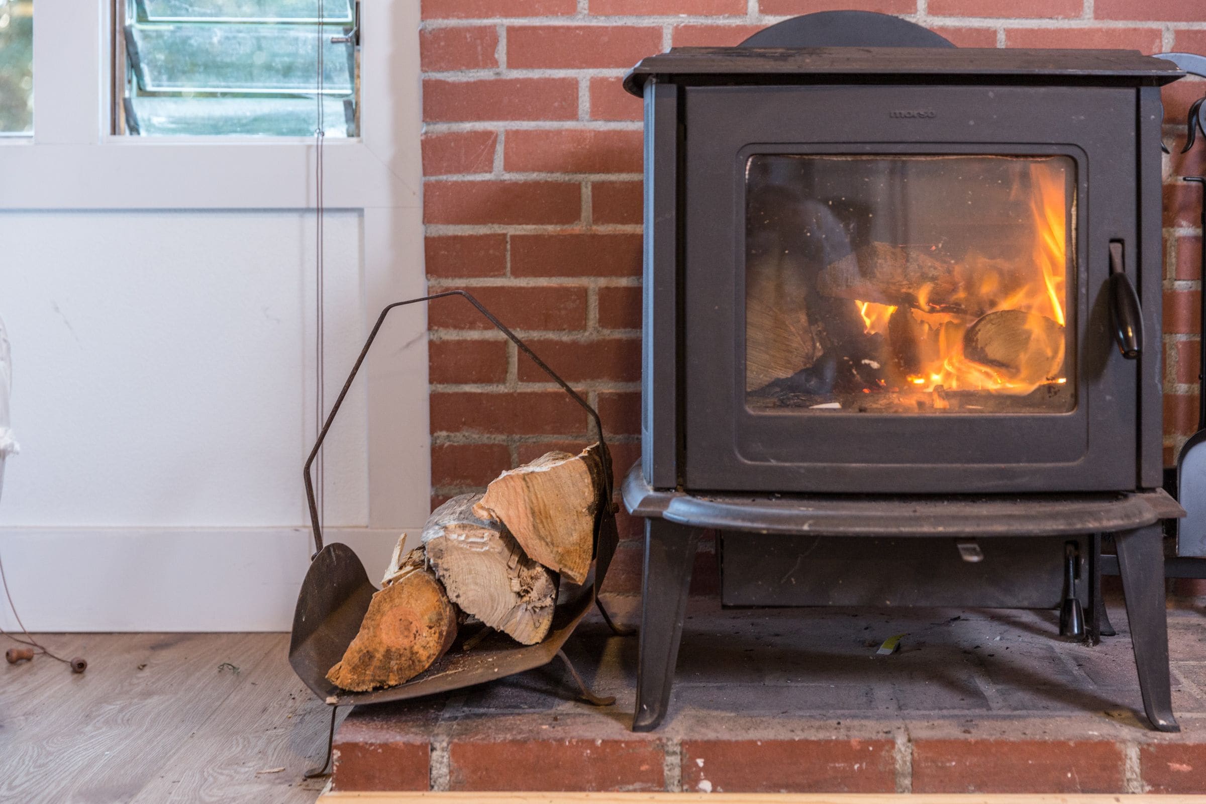 A wood-burning stove next to a brick wall with a window.