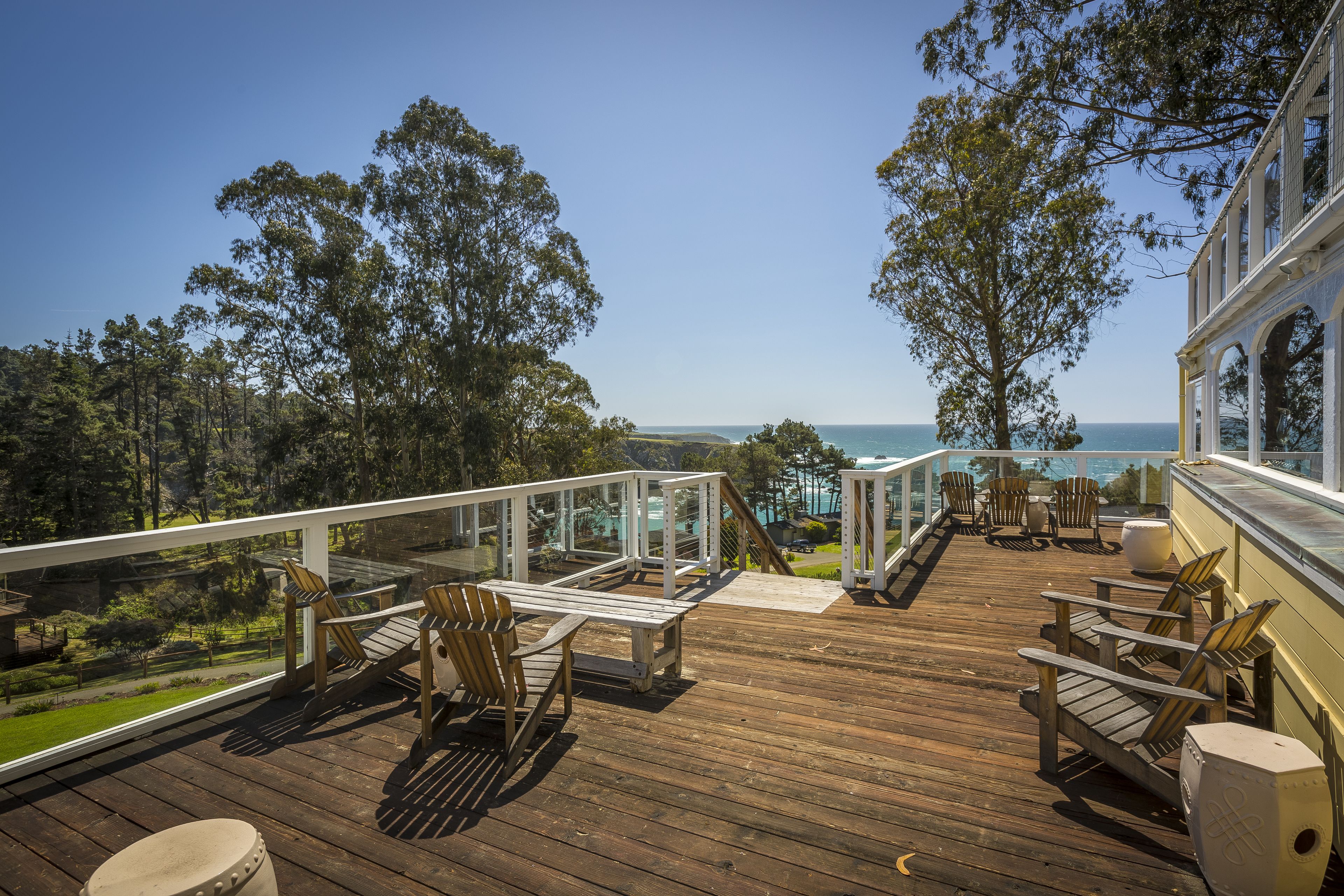 A wooden deck with outdoor furniture, overlooking a scenic view of the ocean and trees.