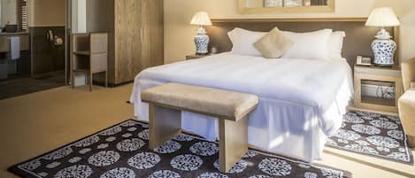 Habitación de hotel con cama, dos mesitas de noche con lámparas, ventilador de techo, espejo grande y vestidor.