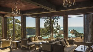 A spacious room with large windows offering ocean views, furnished with sofas and tables, and a chandelier.