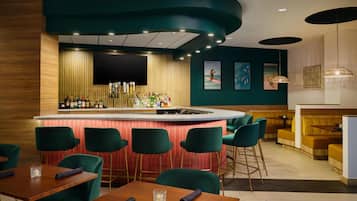 Zona de bar con un mostrador curvo, taburetes de bar verdes y una sala de estar con sofás amarillos.