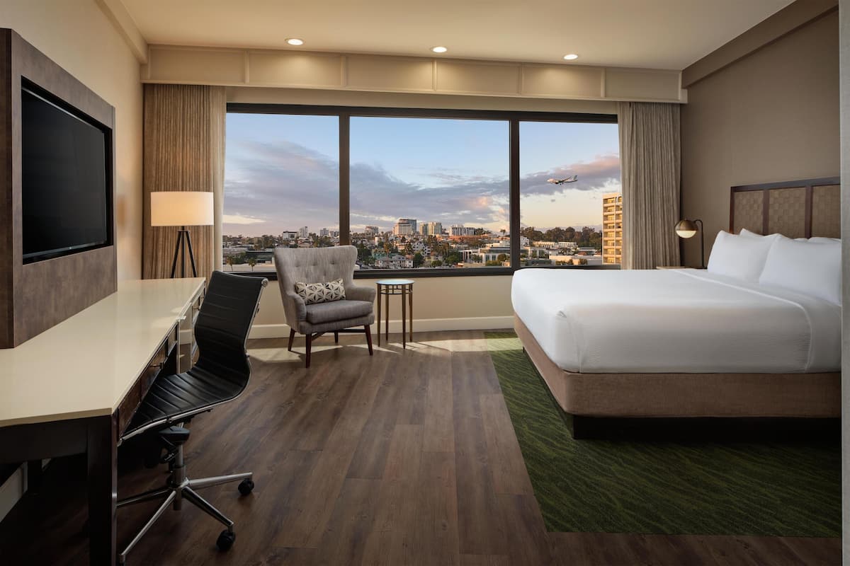 A hotel room with a large bed, a desk, a chair, and a TV.