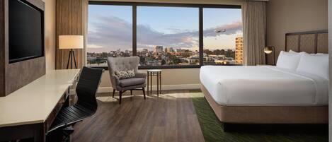 A hotel room with a large bed, a desk, a chair, and a TV.