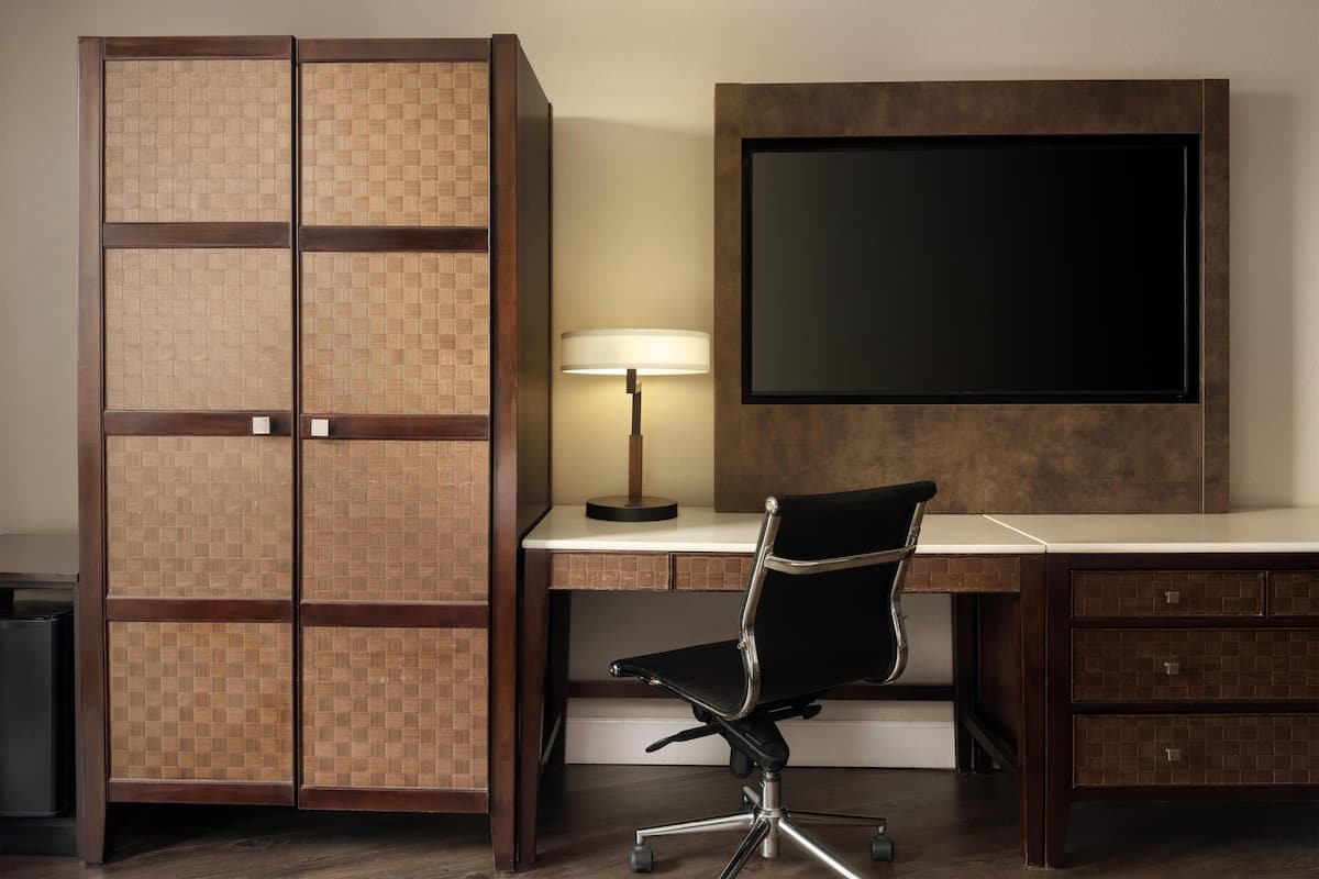 A room with a desk, chair, TV, and a cabinet with a woven pattern.