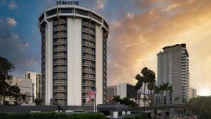 A tall, modern hotel with a curved facade, multiple balconies, and an American flag. - The DEXTRO Little Italy, BW Premier Collection (San Diego)