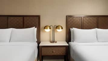 A hotel room with two beds, a nightstand with a lamp, and a wooden headboard.