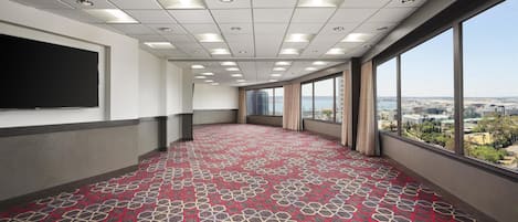 Un salón de conferencias con alfombra estampada, ventanas amplias con vista a la ciudad y una pizarra en la pared.