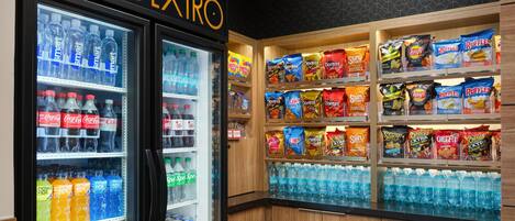 Máquina expendedora de bebidas con diversas opciones y un expositor de aperitivos de varias marcas.