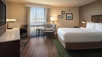 A hotel room with a large bed, a desk, a chair, a TV, a window with curtains, and a lamp.