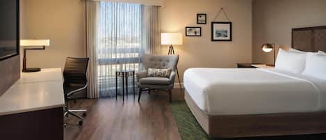 Une chambre d’hôtel avec un grand lit, un bureau, une chaise, une télévision, une fenêtre avec des rideaux et une lampe.