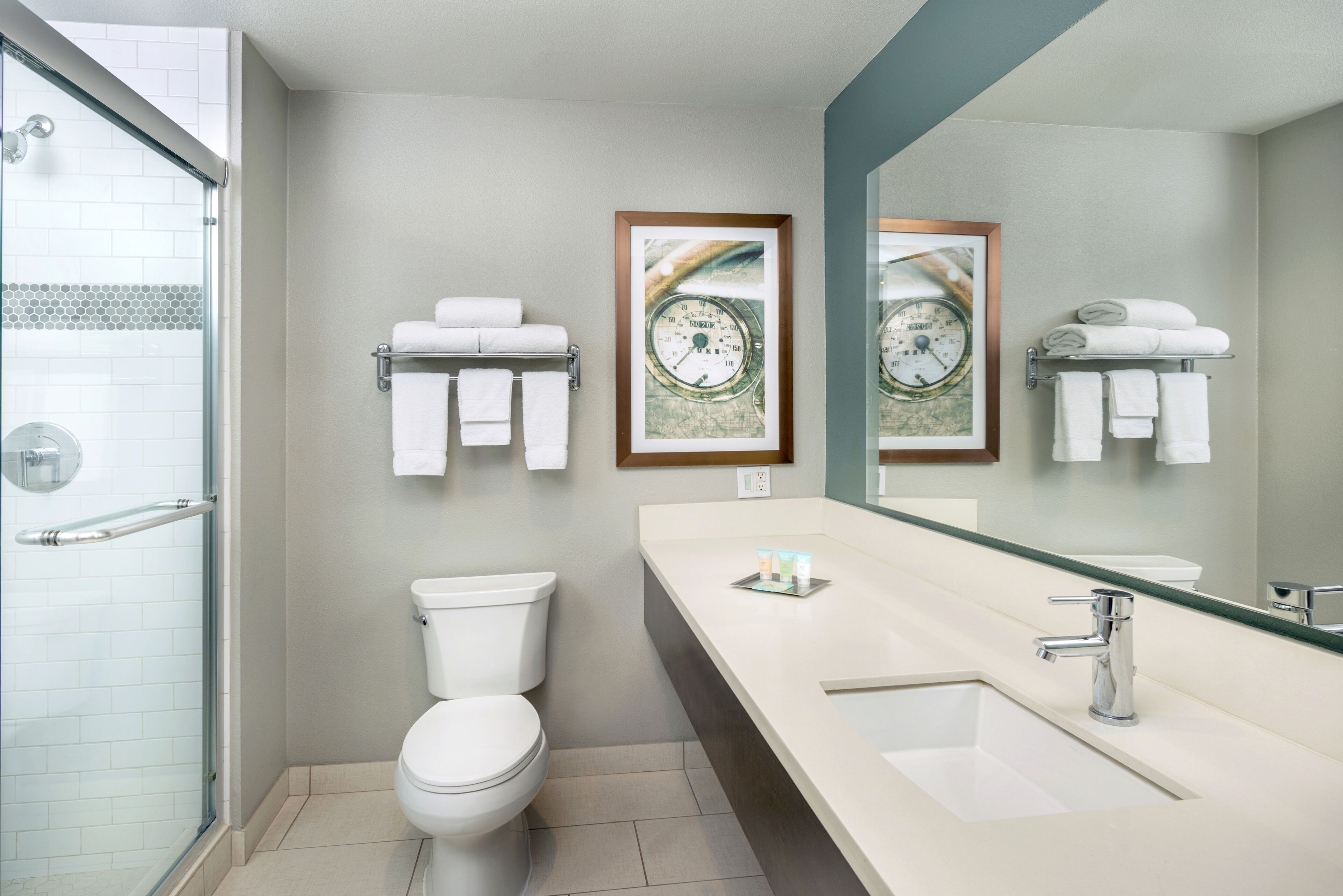 A modern bathroom with a glass shower enclosure, a toilet, a sink with a mirror, and two framed pictures on the wall.