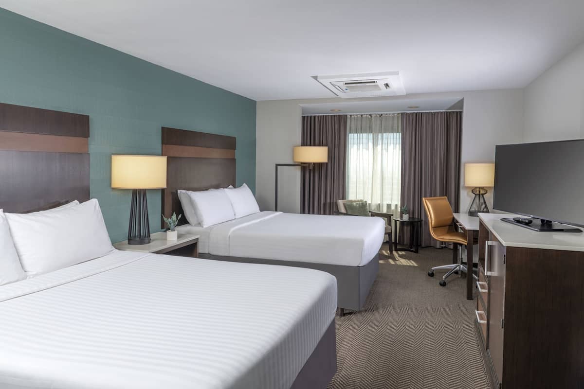 A hotel room with two beds, a desk, a chair, and a TV.