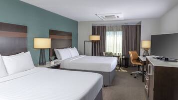 Quarto de hotel com duas camas, uma escrivaninha, uma cadeira e uma televisão.