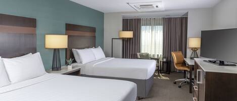 Una habitación de hotel con dos camas, un escritorio, una silla y un televisor.