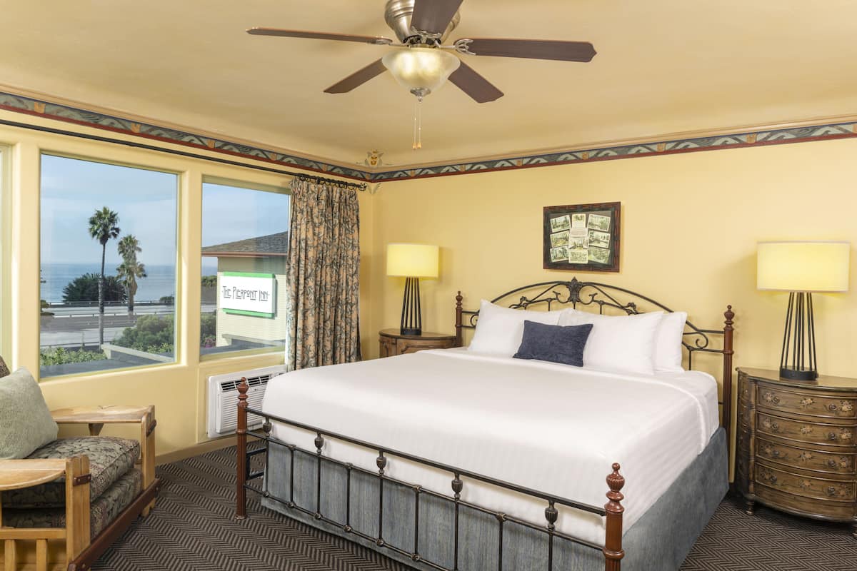 A hotel room with a large bed, two bedside tables, a ceiling fan, and a view of the ocean.