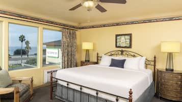 A hotel room with a large bed, two bedside tables, a ceiling fan, and a view of the ocean.