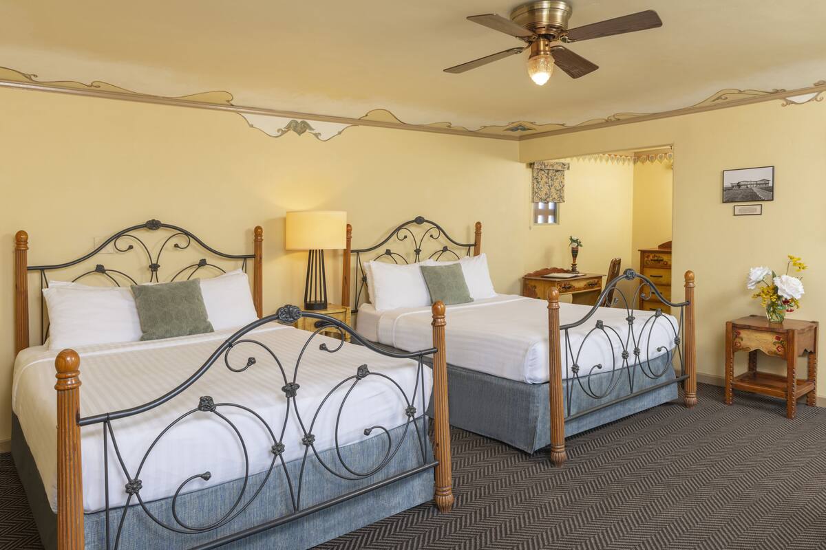 A hotel room with two beds, a ceiling fan, a nightstand, and a small table with a vase of flowers.