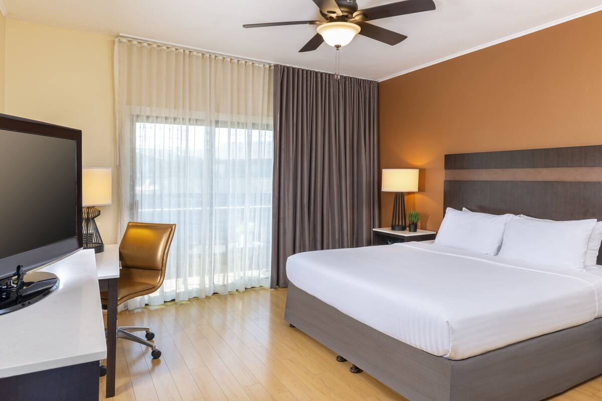 A hotel room with a bed, desk, chair, television, and curtains.