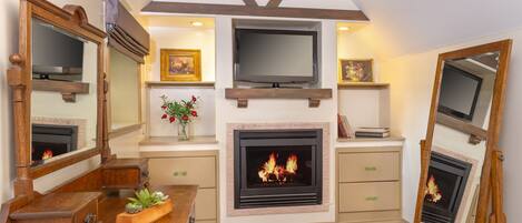 A room with a fireplace, wooden furniture, a television mounted above it, and a mirror on the wall.